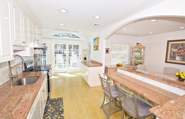 kitchen with arched walkways, a sink, electric range, white cabinetry, and light wood-style flooring