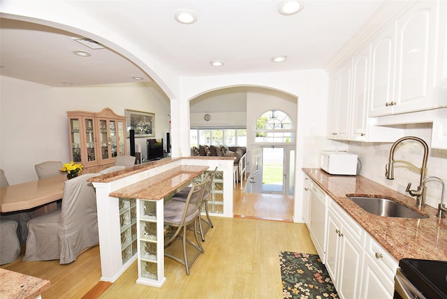 kitchen with a sink, arched walkways, light stone counters, open floor plan, and white cabinets