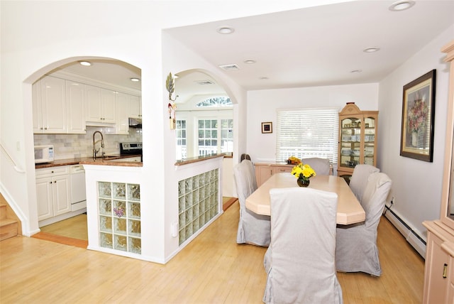 dining space featuring a baseboard radiator, arched walkways, light wood-style flooring, and recessed lighting