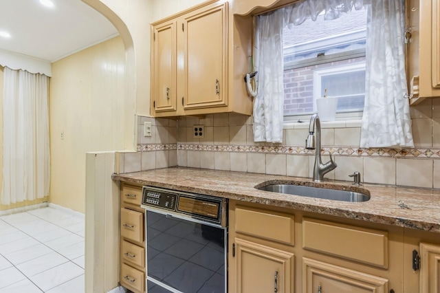 kitchen featuring tasteful backsplash, arched walkways, black dishwasher, a sink, and light stone counters