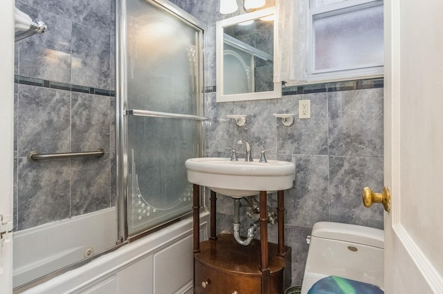full bathroom with toilet, enclosed tub / shower combo, a sink, and tile walls