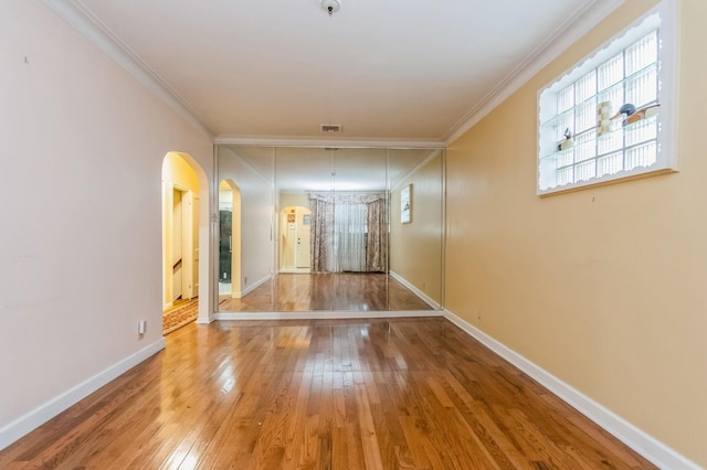 empty room featuring arched walkways, ornamental molding, visible vents, baseboards, and hardwood / wood-style flooring