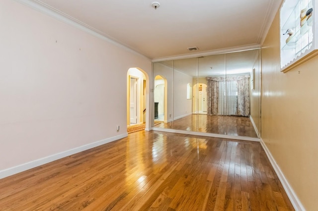 unfurnished room featuring arched walkways, hardwood / wood-style floors, baseboards, and ornamental molding