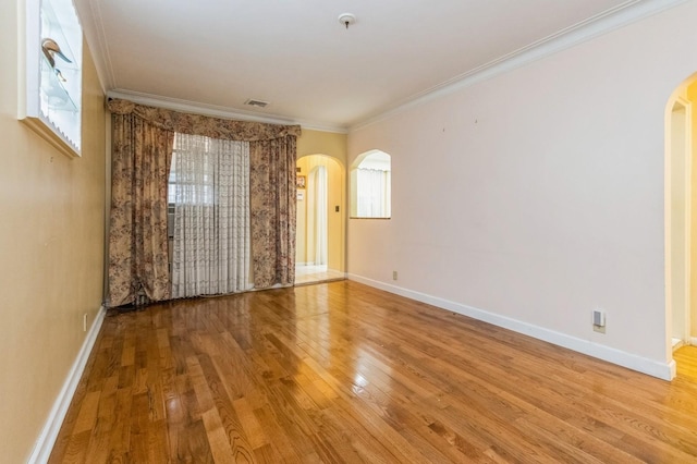 spare room with arched walkways, baseboards, crown molding, and wood finished floors
