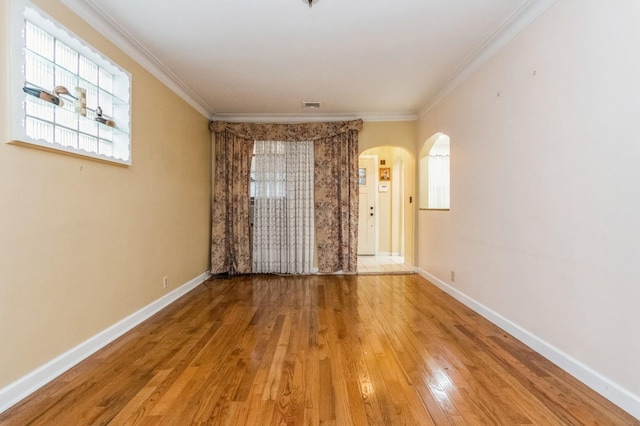 empty room with arched walkways, wood finished floors, baseboards, and ornamental molding