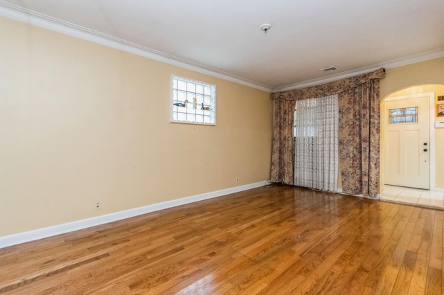 unfurnished room with light wood-style flooring, arched walkways, ornamental molding, visible vents, and baseboards