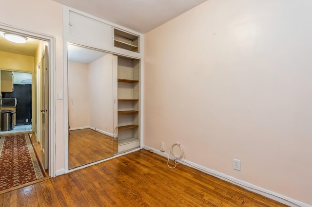 unfurnished bedroom featuring a closet, baseboards, freestanding refrigerator, and hardwood / wood-style floors
