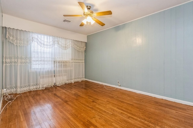 unfurnished room featuring baseboards, a ceiling fan, visible vents, hardwood / wood-style floors, and radiator