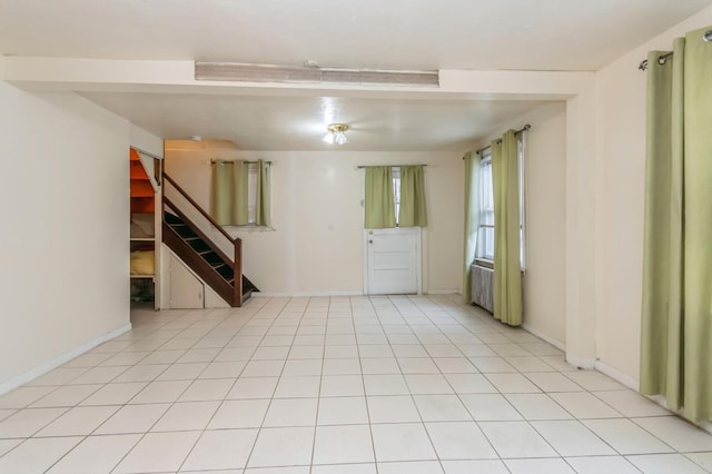 empty room with light tile patterned floors, baseboards, and stairs