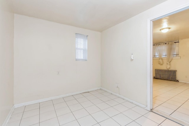 empty room featuring radiator heating unit, light tile patterned floors, and baseboards