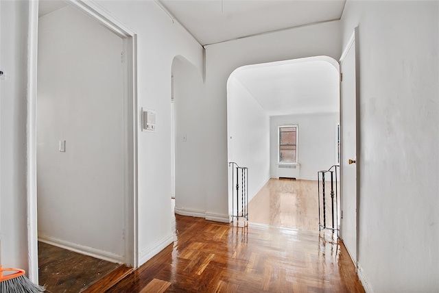 hall with arched walkways, radiator heating unit, and baseboards