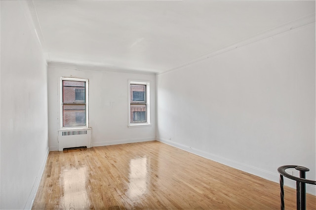 empty room with ornamental molding, radiator heating unit, wood finished floors, and baseboards