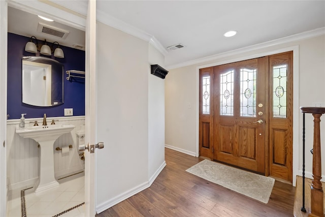 foyer with baseboards, wood finished floors, visible vents, and crown molding