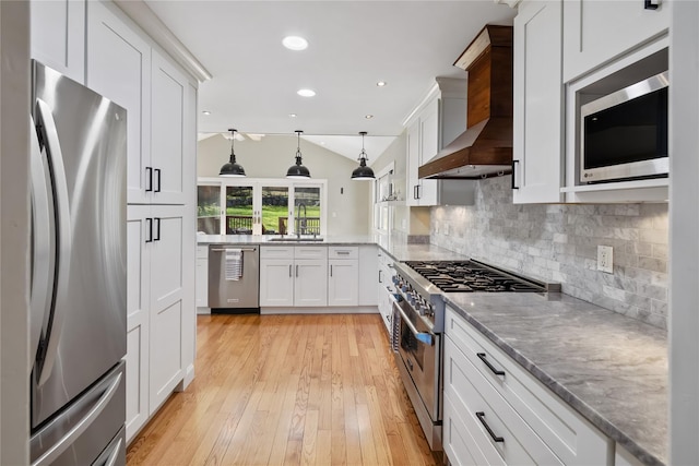 kitchen with wall chimney exhaust hood, stainless steel appliances, white cabinets, and a sink