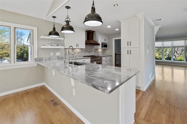 kitchen with a sink, a wealth of natural light, baseboards, wall chimney exhaust hood, and appliances with stainless steel finishes