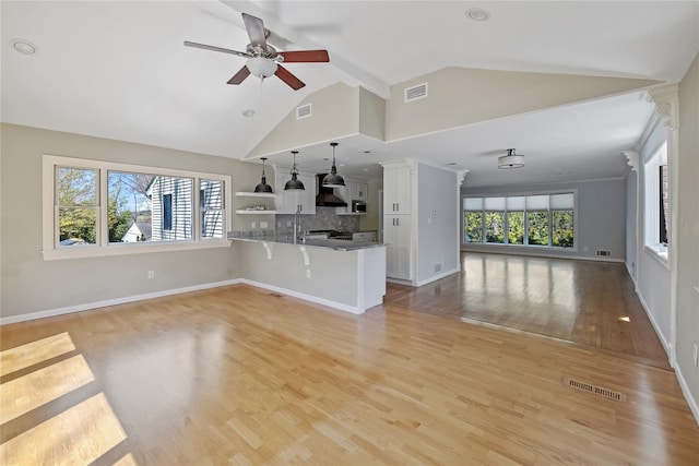 unfurnished living room with light wood-type flooring, a ceiling fan, visible vents, and vaulted ceiling