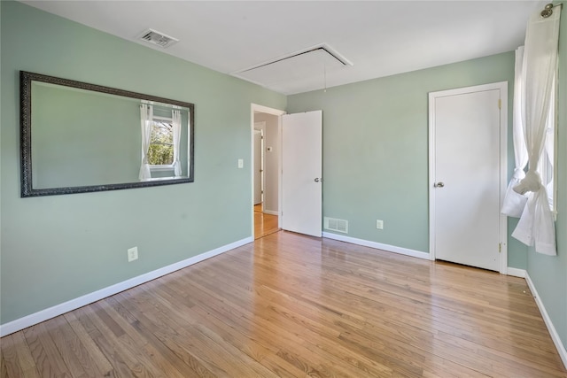empty room with attic access, wood finished floors, visible vents, and baseboards