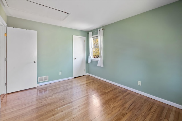unfurnished room with attic access, wood finished floors, visible vents, and baseboards