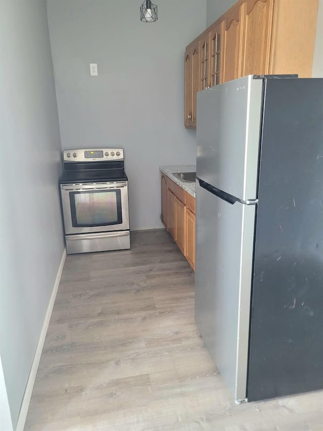 kitchen featuring baseboards, a sink, light wood-style floors, brown cabinetry, and stainless steel appliances
