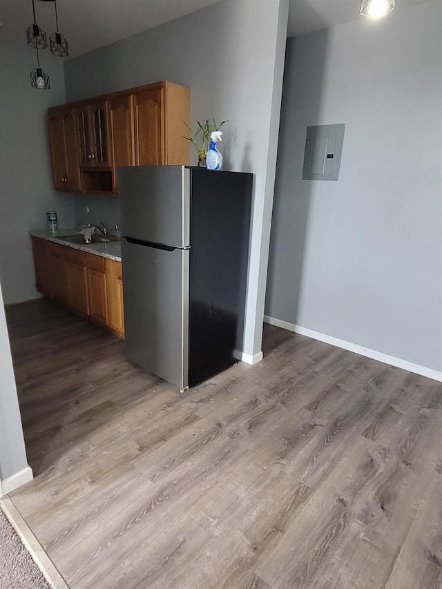 kitchen featuring baseboards, electric panel, freestanding refrigerator, light stone countertops, and light wood-style floors