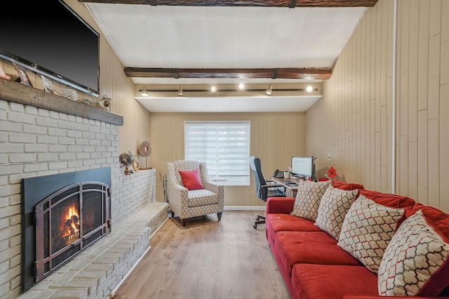 living area with beamed ceiling, wooden walls, wood finished floors, and a brick fireplace