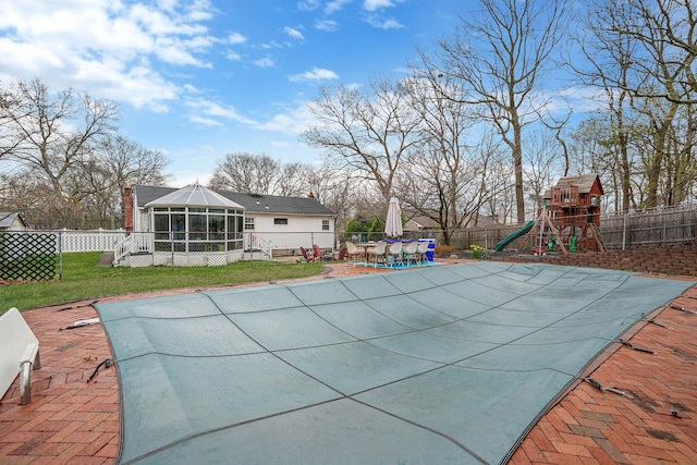 view of swimming pool with a sunroom, a patio area, a lawn, a fenced backyard, and a playground