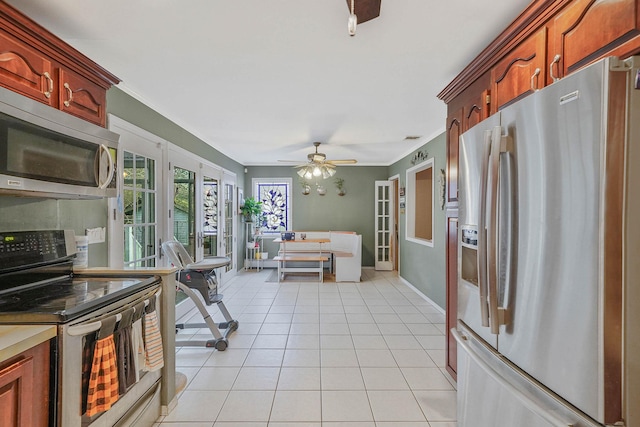 kitchen featuring crown molding, light tile patterned flooring, ceiling fan, baseboards, and appliances with stainless steel finishes