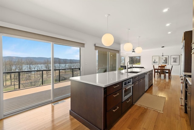 kitchen with a sink, light countertops, dark brown cabinetry, a center island with sink, and stainless steel oven