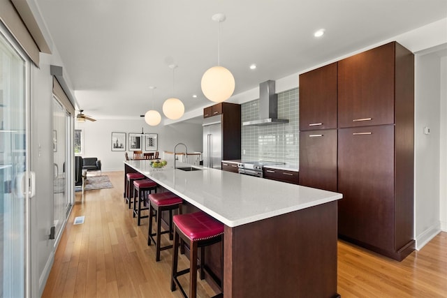 kitchen featuring modern cabinets, wall chimney range hood, light wood-style floors, and stainless steel appliances