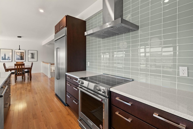 kitchen with wall chimney range hood, backsplash, light wood-style floors, modern cabinets, and stainless steel appliances