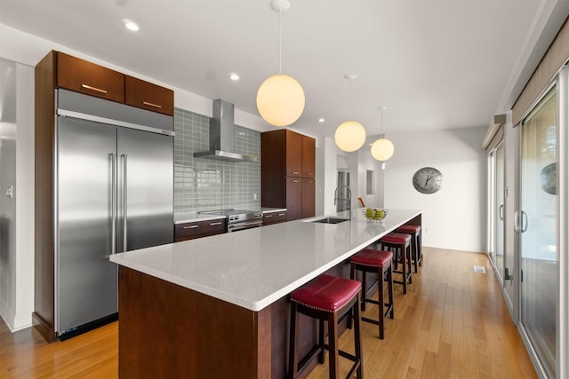 kitchen featuring modern cabinets, wall chimney exhaust hood, stainless steel appliances, and light wood-style flooring