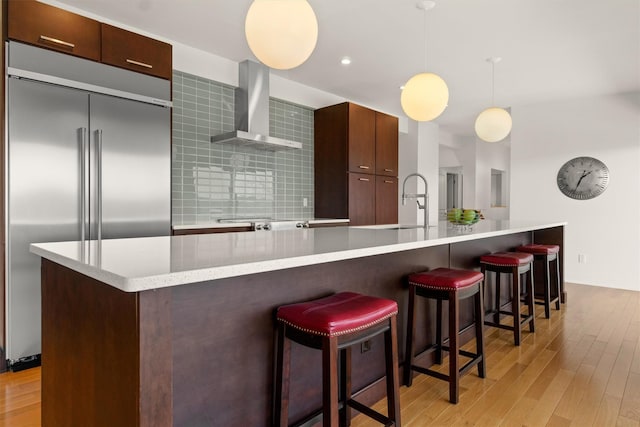 kitchen with appliances with stainless steel finishes, light wood finished floors, wall chimney range hood, and modern cabinets