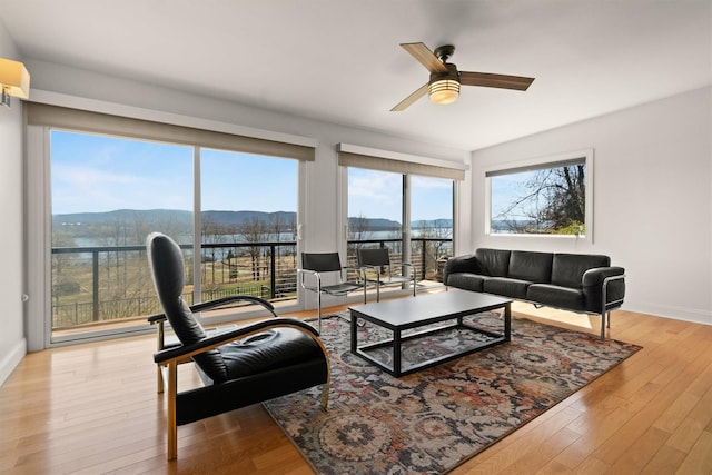 living room featuring ceiling fan, baseboards, a water and mountain view, and wood finished floors