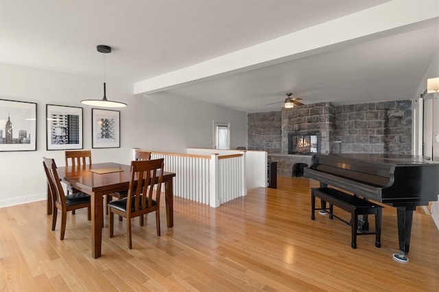 dining space featuring light wood-style floors, a stone fireplace, and a ceiling fan
