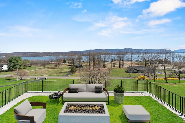 view of home's community with fence, a water and mountain view, a yard, and an outdoor living space with a fire pit