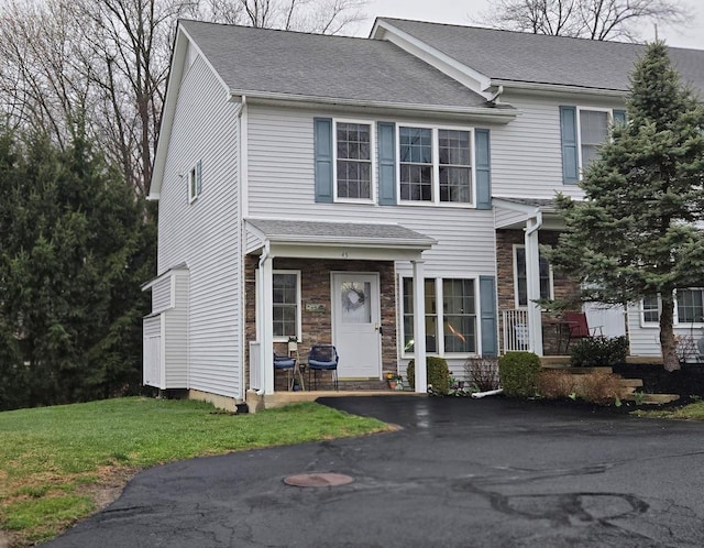 view of front of home featuring a front lawn, a shingled roof, and stone siding