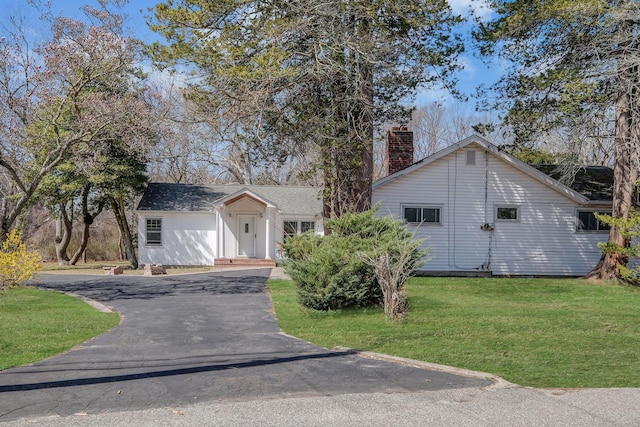 ranch-style home with a chimney, driveway, and a front lawn