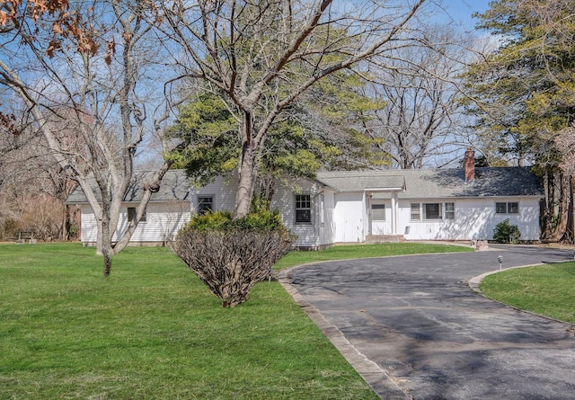 ranch-style home featuring a chimney, driveway, and a front yard