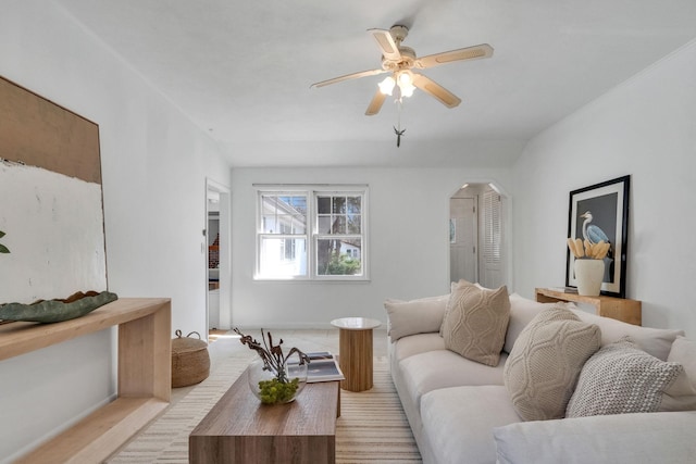 living room with arched walkways, light wood-type flooring, baseboards, and ceiling fan