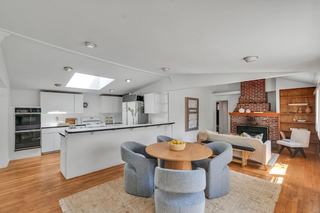 dining area with light wood finished floors, lofted ceiling with skylight, and a brick fireplace