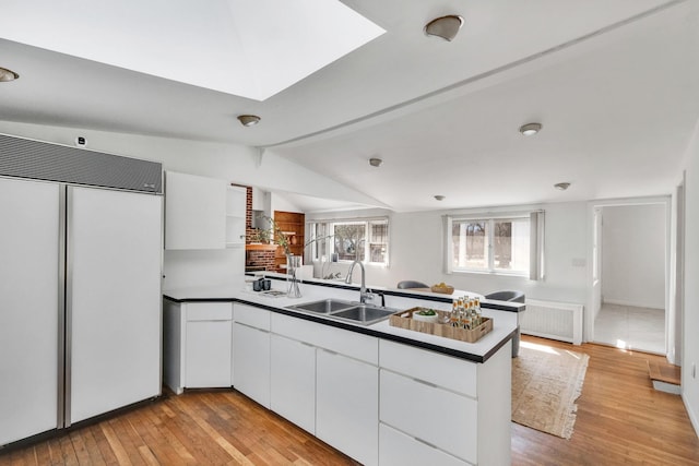 kitchen featuring a sink, a peninsula, built in fridge, light wood finished floors, and white cabinetry