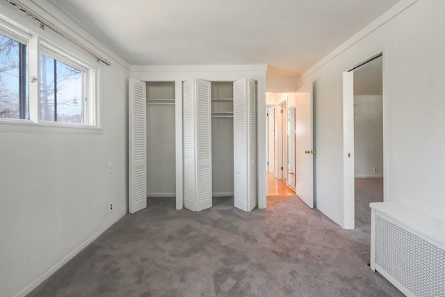 unfurnished bedroom with radiator heating unit, carpet, and multiple closets