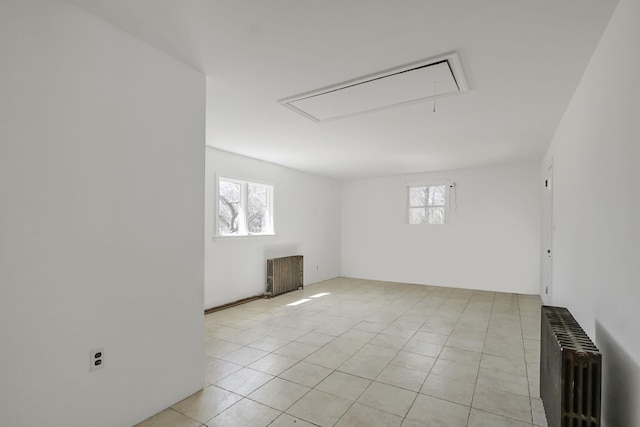 empty room featuring light tile patterned floors, attic access, radiator, and a healthy amount of sunlight