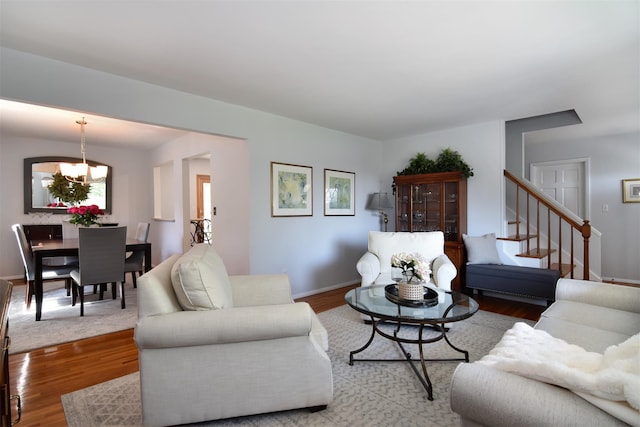 living room featuring wood finished floors, baseboards, a notable chandelier, and stairs