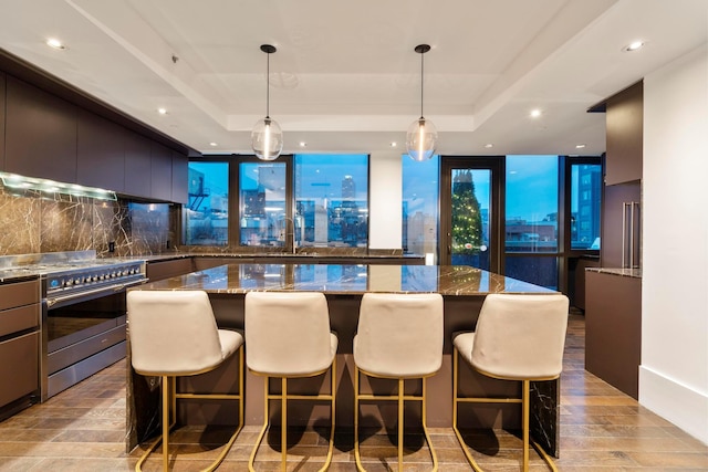 kitchen featuring high end stove, tasteful backsplash, a center island, a raised ceiling, and light wood finished floors