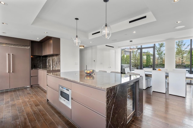 kitchen featuring modern cabinets, a tray ceiling, tasteful backsplash, dark wood-style flooring, and built in appliances