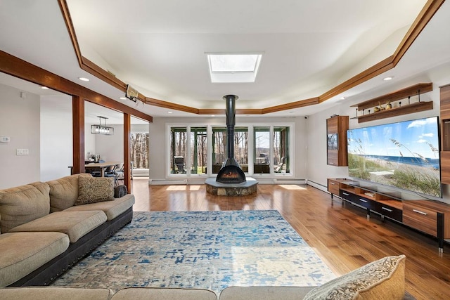 living area featuring a baseboard heating unit, a raised ceiling, a wood stove, a skylight, and wood finished floors