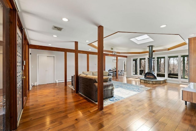 living area with a tray ceiling, a baseboard radiator, wood-type flooring, and visible vents