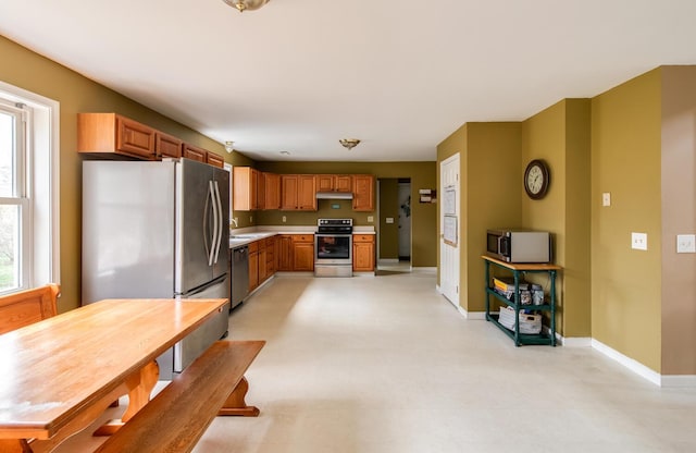kitchen featuring baseboards, light floors, light countertops, under cabinet range hood, and stainless steel appliances