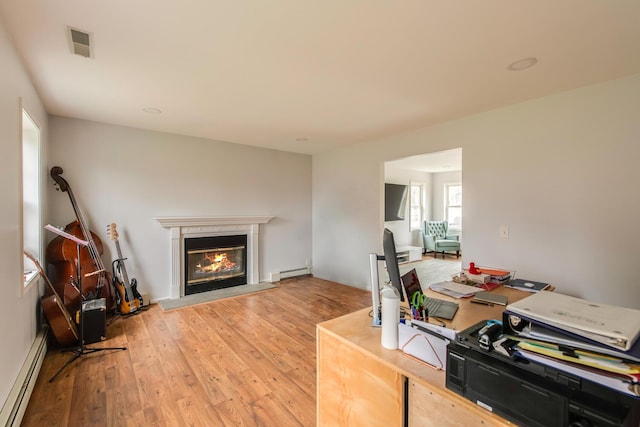 office space featuring visible vents, a glass covered fireplace, a baseboard heating unit, a baseboard radiator, and light wood finished floors